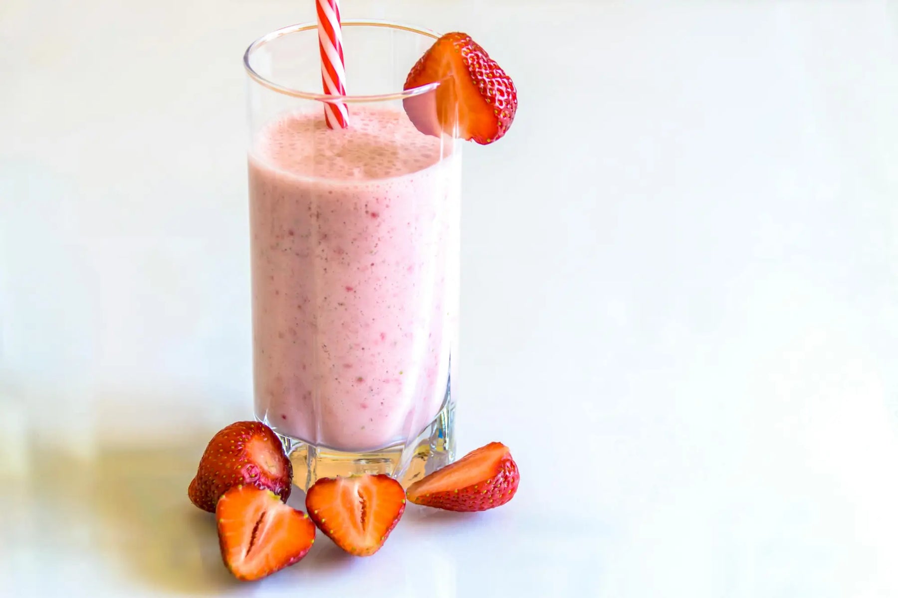 Glass of strawberry smoothie with fresh strawberries and striped straw