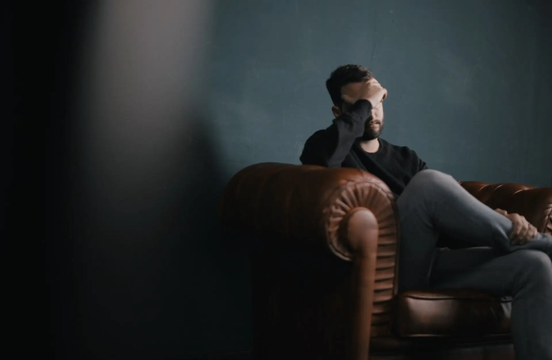 Man holding his head while sat on a sofa