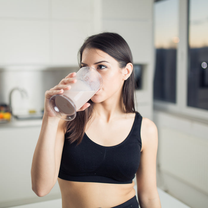 Woman in sportswear drinking sweet banana chocolate protein powder milkshake smoothie.Drinking protein after workout.Whey,banana and low fat milk sport nutrition diet after gym.Healthy lifestyle