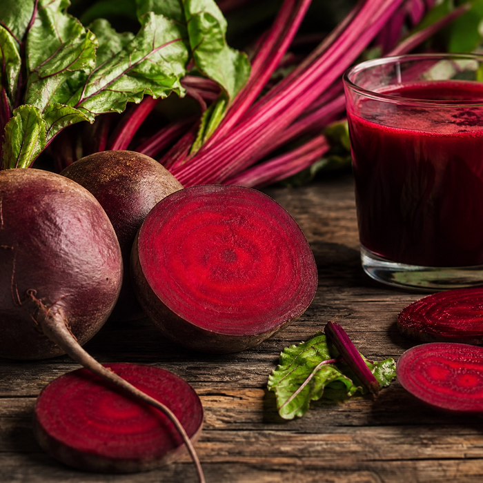Fresh whole and halved beetroots with leafy tops, sliced beetroot rounds and a glass of deep red beetroot juice on wood