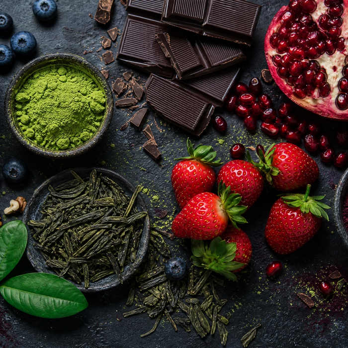 Antioxidant-rich foods including blueberries, pomegranate, dark chocolate, matcha powder and strawberries on dark slate