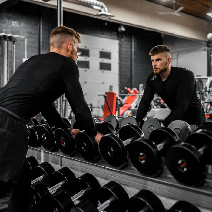 man in black pants and black long sleeve shirt carrying black dumbbells
