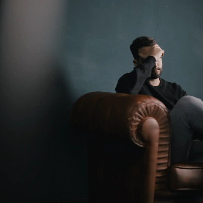 Man holding his head while sat on a sofa
