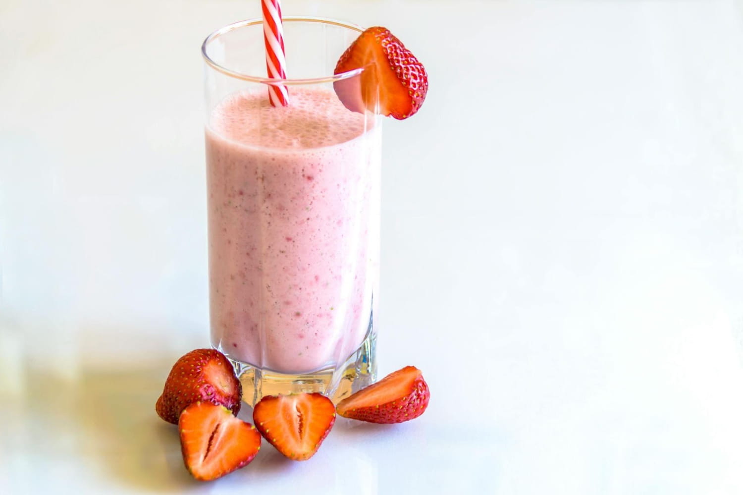Glass of strawberry smoothie with fresh strawberries and striped straw